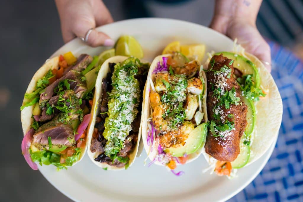 A hand presents a plate containing three appetizing tacos, showcasing a delightful meal.